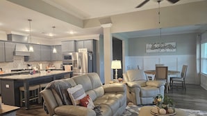 A modern living room with a sofa, ottoman, and a dining area with a table and chairs. - Masters Tournament Rental 2027 (Graniteville)
