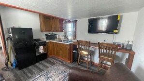 A compact kitchen with a refrigerator, stove, microwave, and sink. There is a dining area with two wooden chairs and a TV mounted on the wall. - Charming 2-bedroom cabin with WiFi and AC in Licking (Licking)