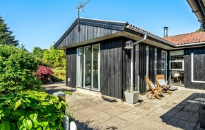 A modern house with a dark exterior, large windows, and a tiled patio area with outdoor furniture.
