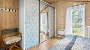 A bedroom with wooden walls, a large mirror, a bed with a striped blanket, and a view of greenery outside.