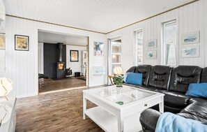 A living room with a black leather sofa, white walls, wooden flooring, a glass coffee table, and a fireplace.