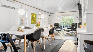 A modern dining area with a white table, black and white chairs, and a large window offering a view of greenery outside.