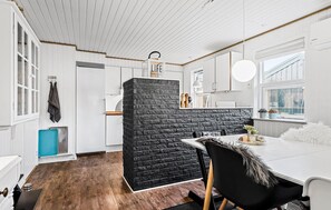 A modern kitchen with white cabinetry, a black brick accent wall, and a dining area with a white table and chairs.
