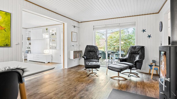A modern interior with a wooden floor, black leather chairs, a dining area, and a view through large windows.