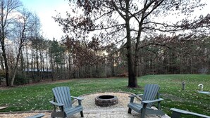 An outdoor seating area with Adirondack chairs and a stone fire pit surrounded by a stone patio.
