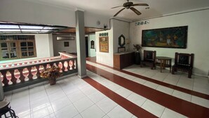 A spacious lobby with a reception desk, a ceiling fan, a painting on the wall, and a tiled floor with a red stripe. - Hotel Candra Adigraha (Denpasar)