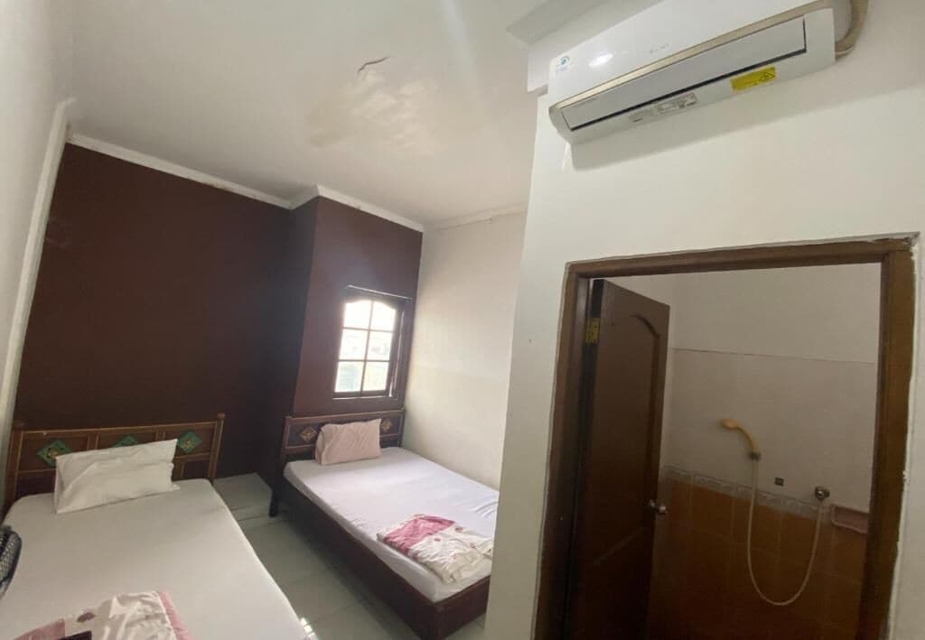 A small, compact room with a single bed, a window, an air conditioning unit, and a shower area.