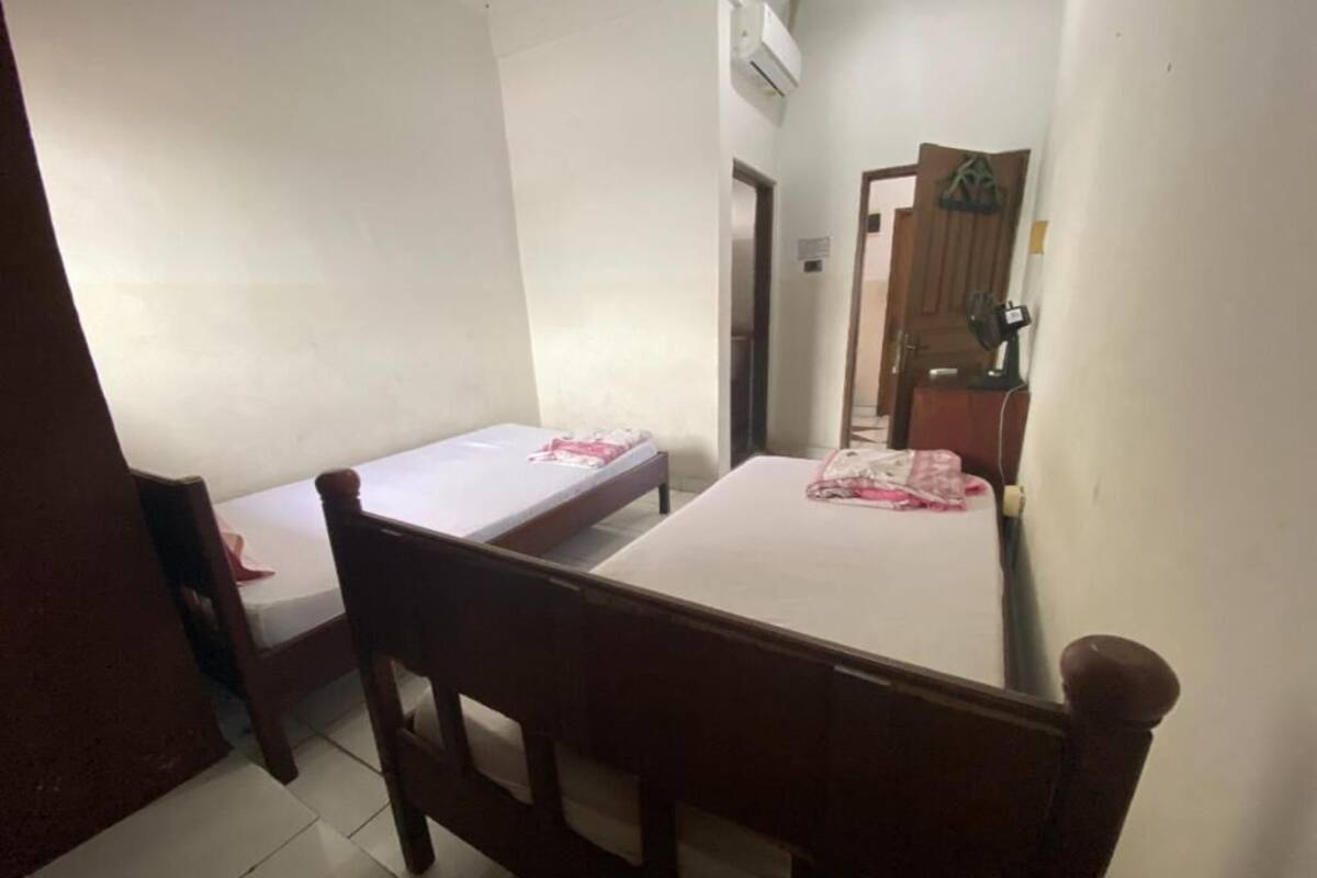 A small, simple room with a single bed, a wooden chair, and a small table.