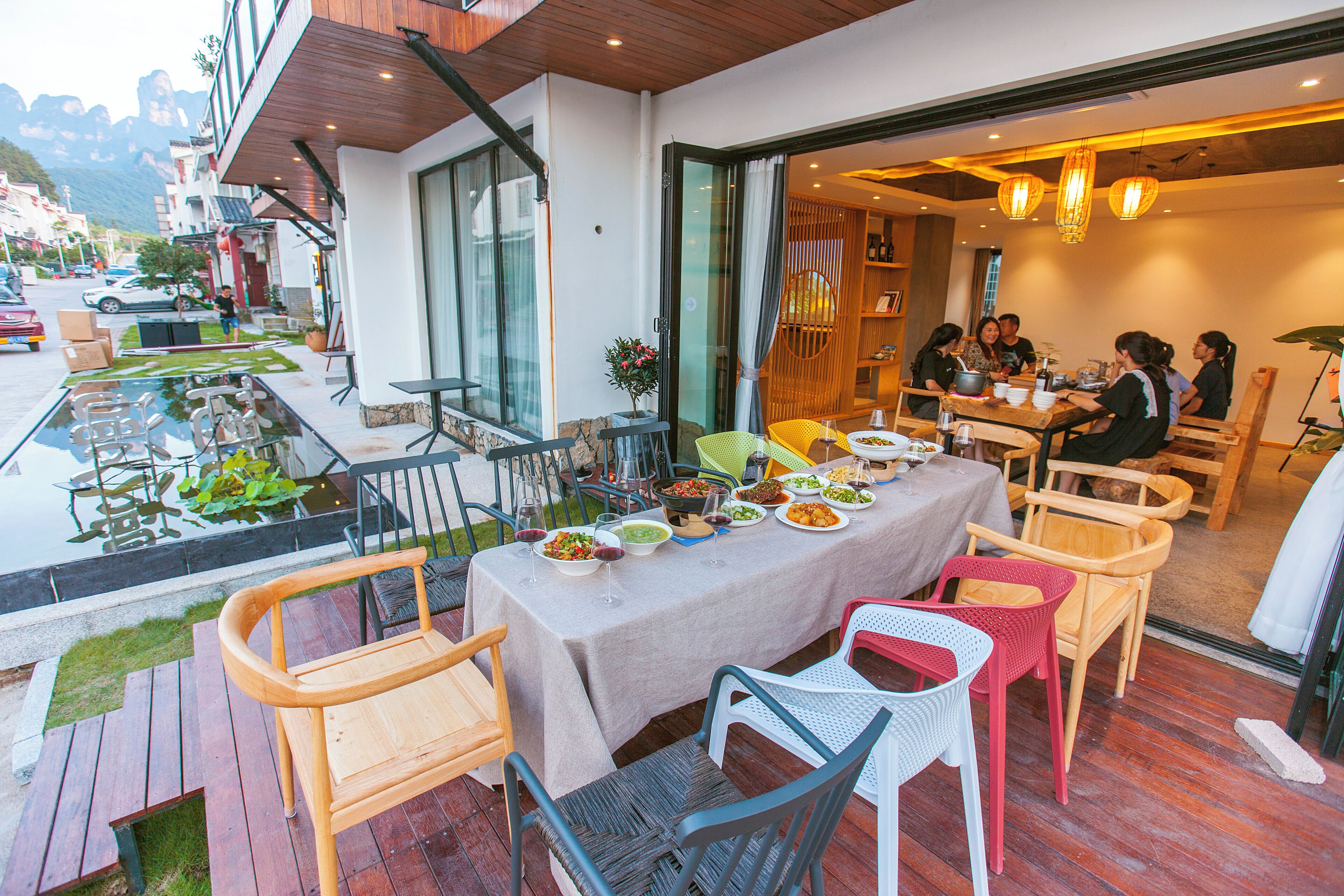 An outdoor dining area with a table set for a meal, surrounded by various chairs and a small garden.