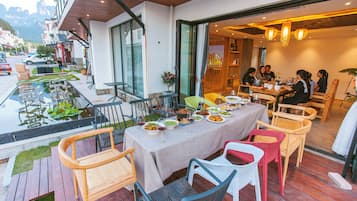 An outdoor dining area with a table set for a meal, surrounded by various chairs and a small garden.