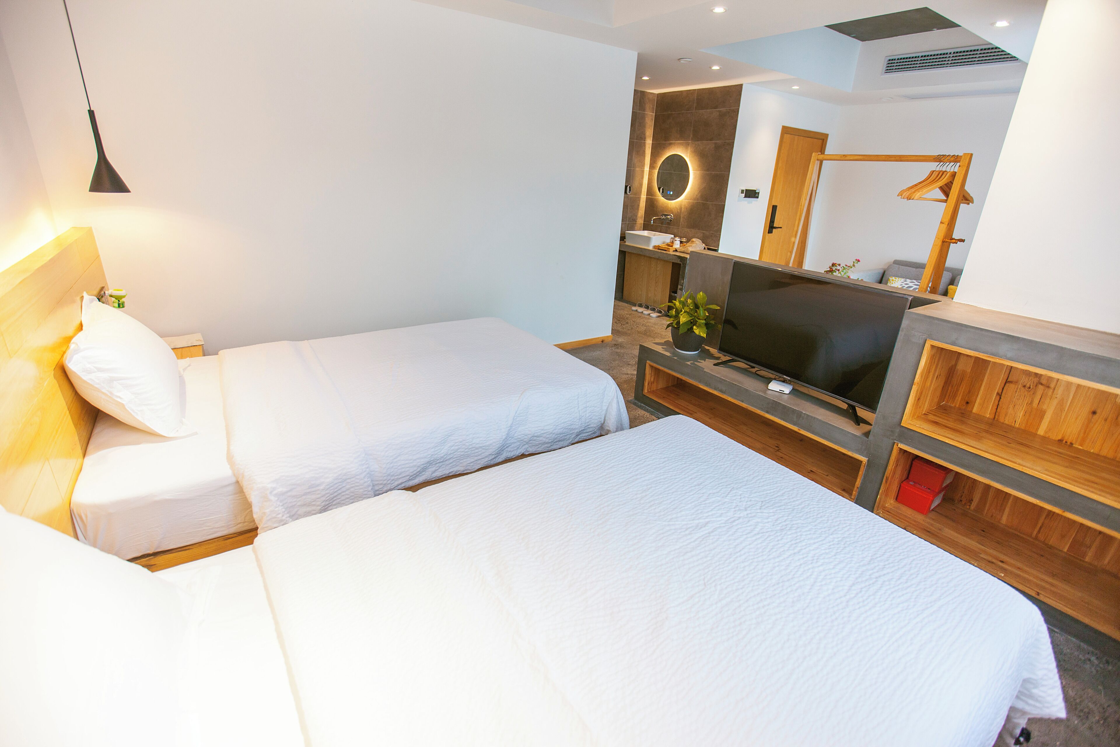 Habitació d'hotel amb dos llits, televisió, mirall i un armari de fusta.