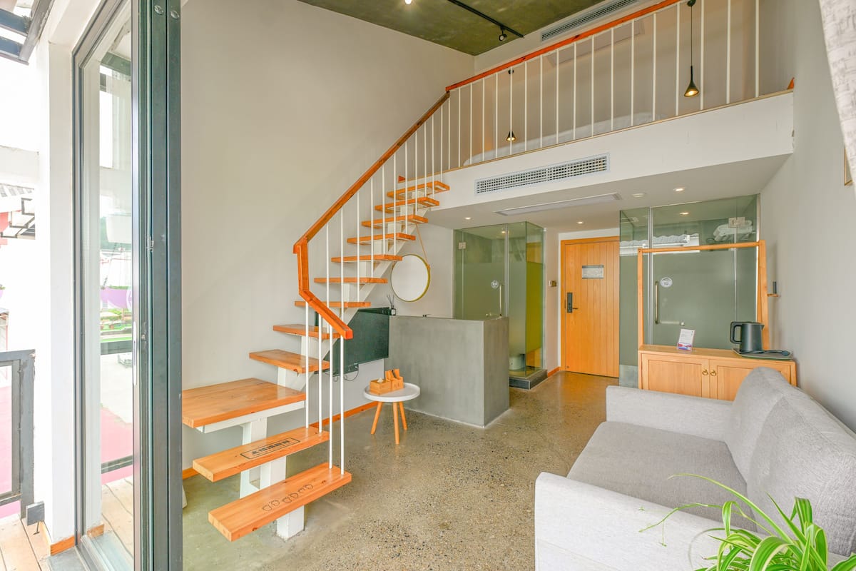 A modern interior with a wooden staircase, a reception desk, a sofa, and a kitchen area.