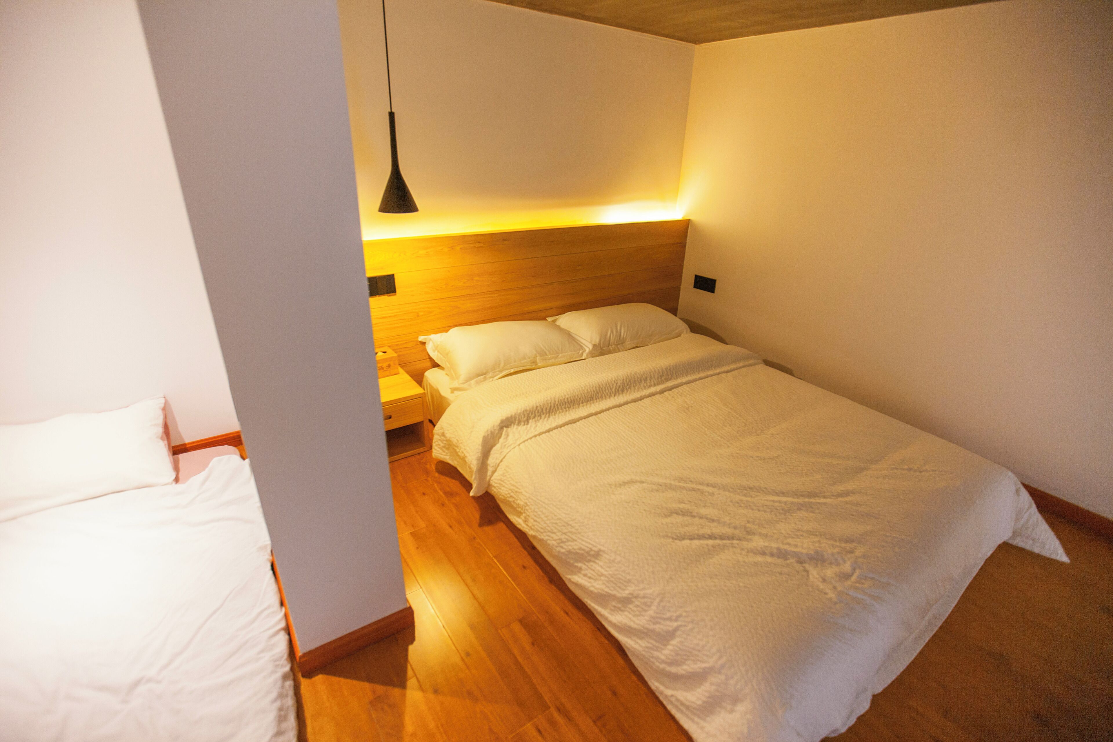 Een slaapkamer met een houten hoofdbord, een witte dekbedovertrek en een nachtkastje met een lamp.