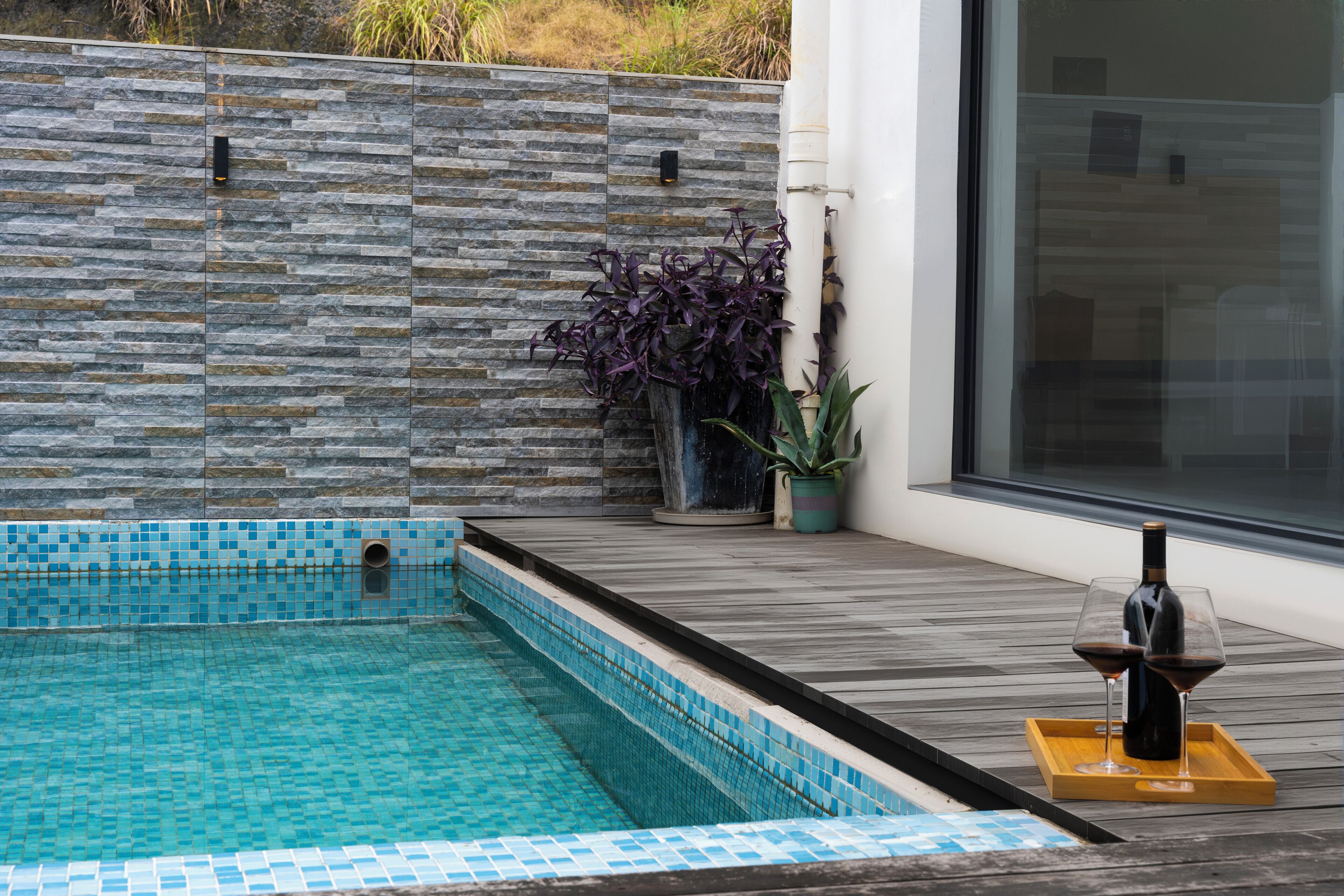 A swimming pool with stone tiles, a wooden deck, and a potted plant.