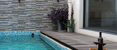 Une piscine aux bords recouverts de pierres, une terrasse en bois et une plante en pot.