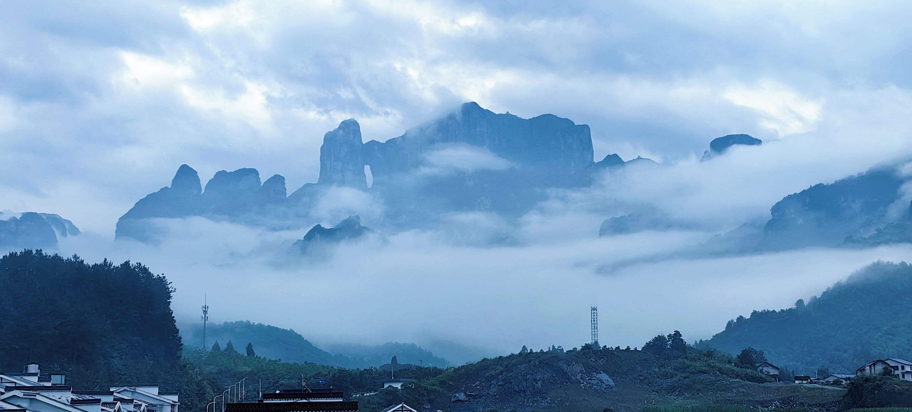 A mountainous landscape with a prominent peak, surrounded by clouds and vegetation.