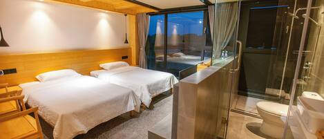 A modern hotel room with two beds, a glass-enclosed shower, and a view of the mountains.