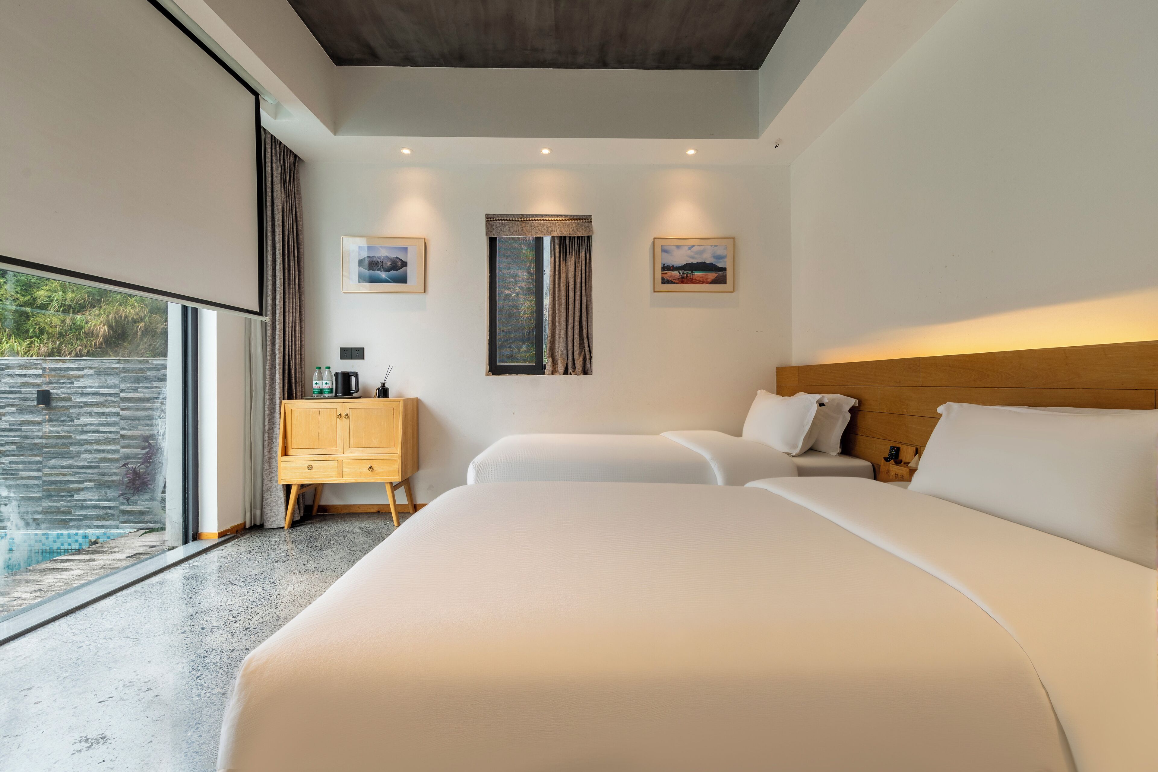 A modern hotel room with a large bed, a wooden dresser, and a view of a swimming pool.