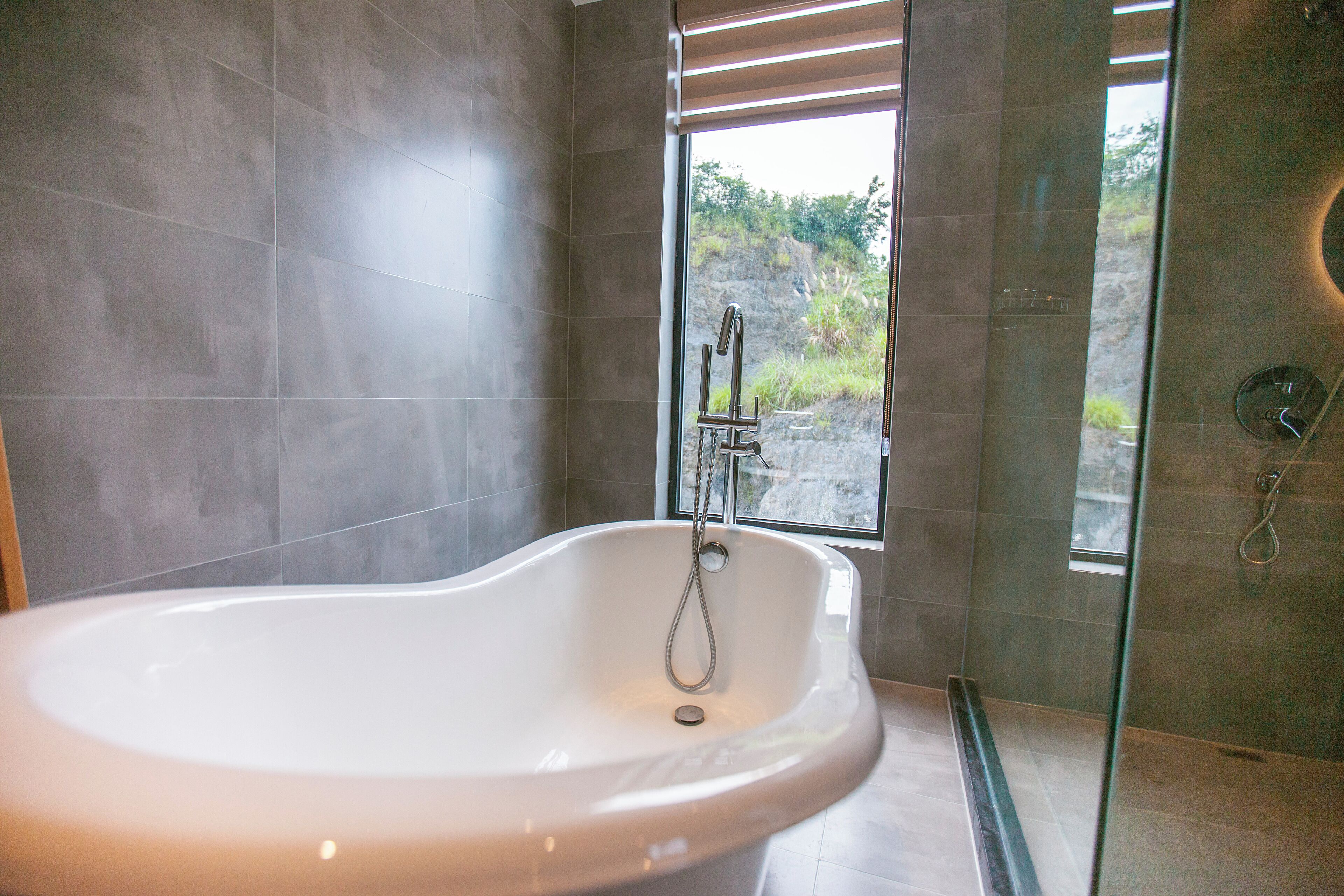 A modern bathroom with a freestanding bathtub, a glass shower enclosure, and a view of a rocky landscape through a window.