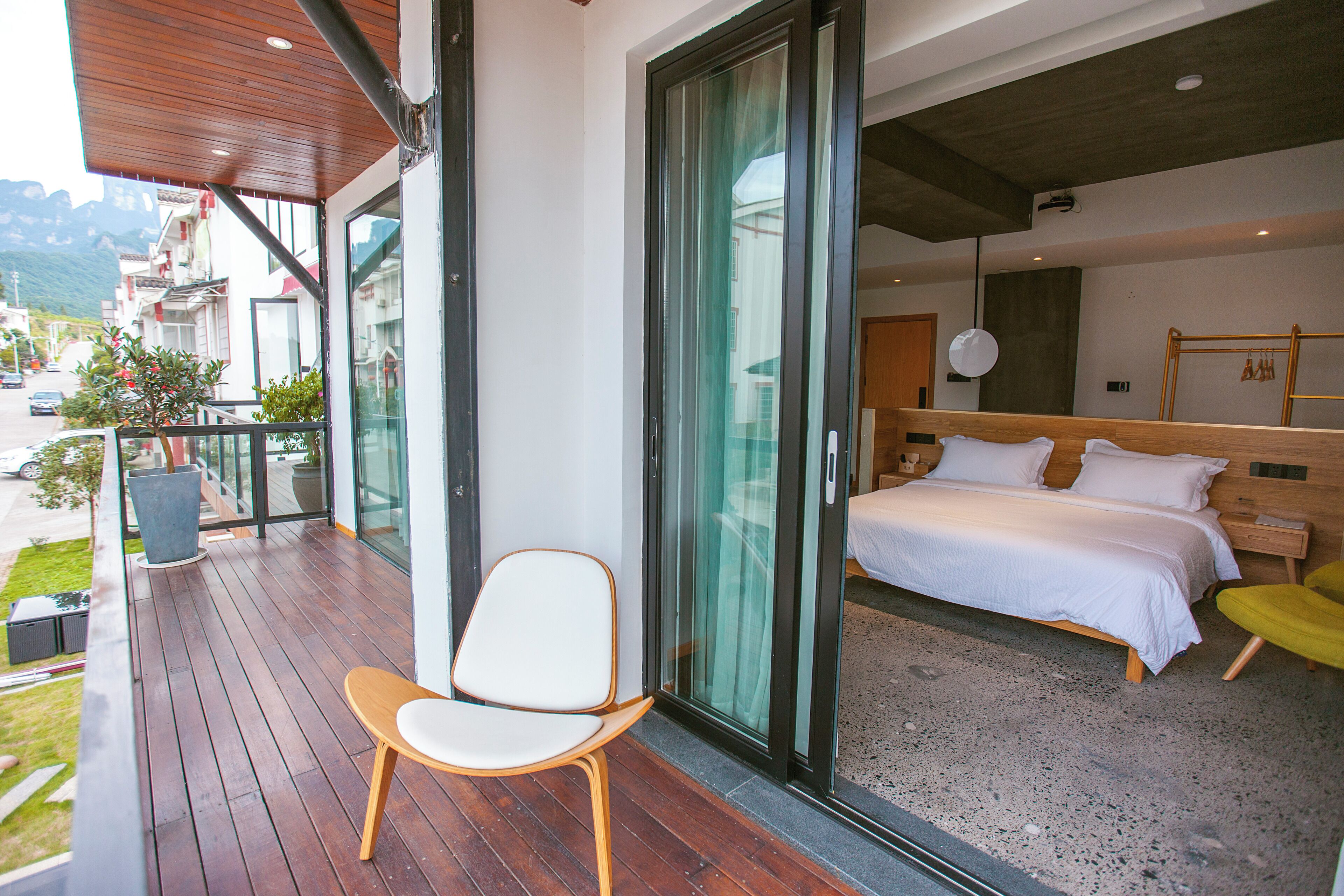 A modern hotel room with a balcony, a bed, a chair, and a view of the outside.