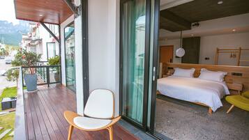 A modern hotel room with a balcony, a bed, a chair, and a view of the outside.