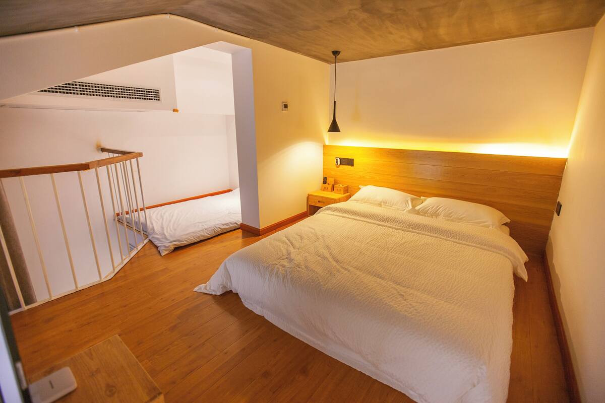 A bedroom with a wooden bed, a nightstand, a wall-mounted lamp, and a staircase leading to an upper level.