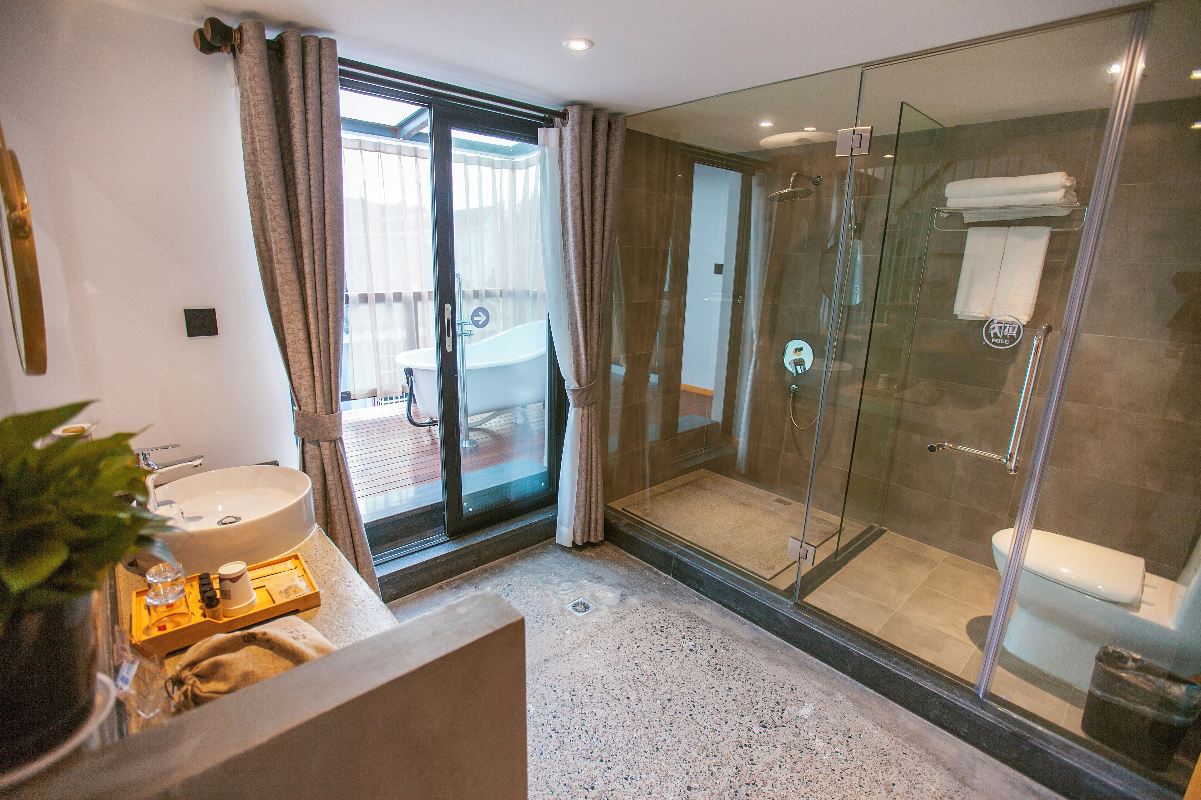 A modern bathroom with a glass-enclosed shower, a large sink, and a glass door leading to an outdoor area.