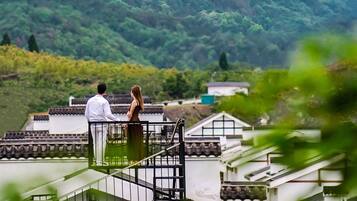 Una pareja está de pie en un balcón con vistas a un paisaje montañoso.