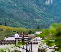 Una pareja está de pie en un balcón con vistas a un paisaje montañoso.