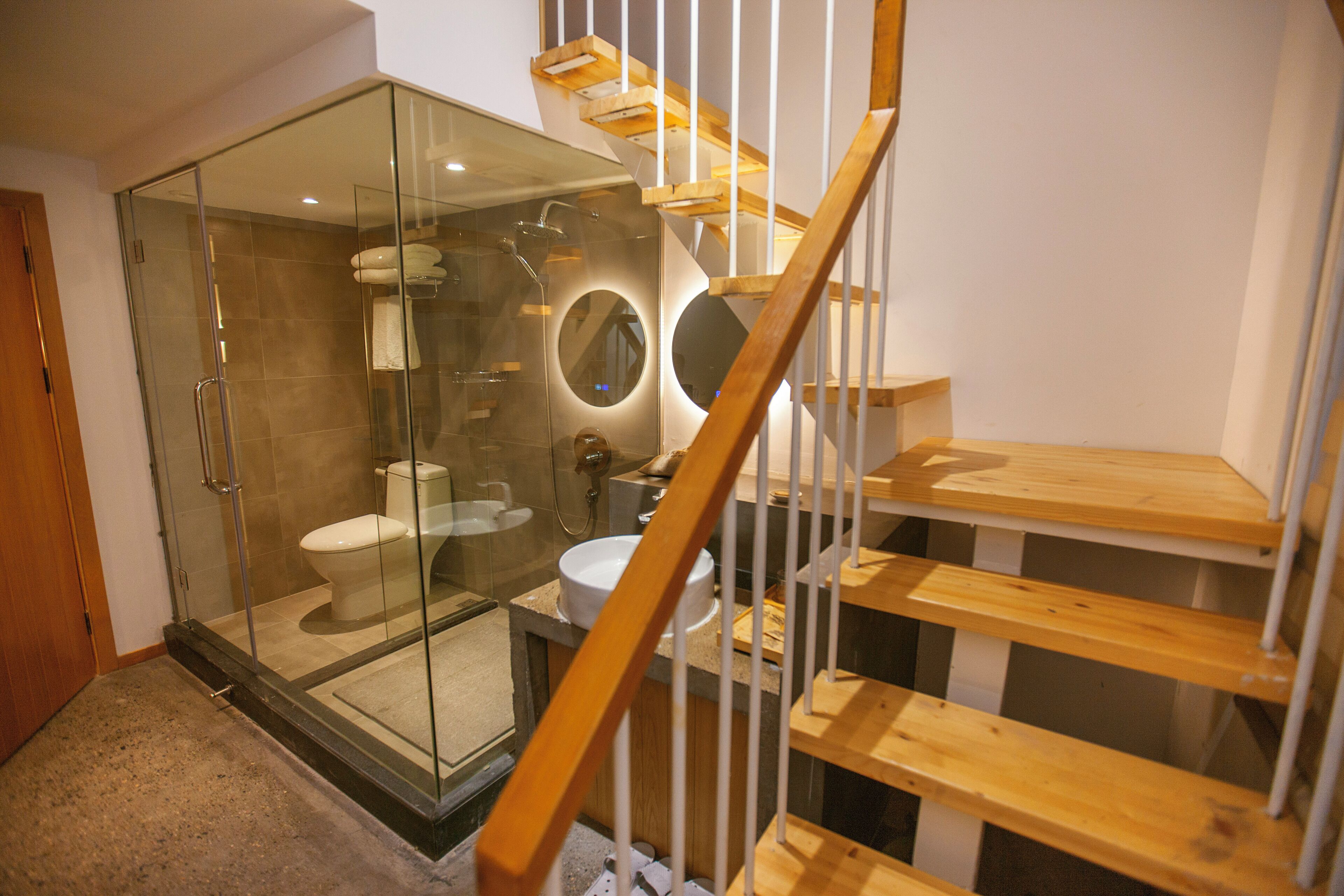 Une salle de bain moderne avec une douche à parois de verre, un escalier en bois et un lavabo.