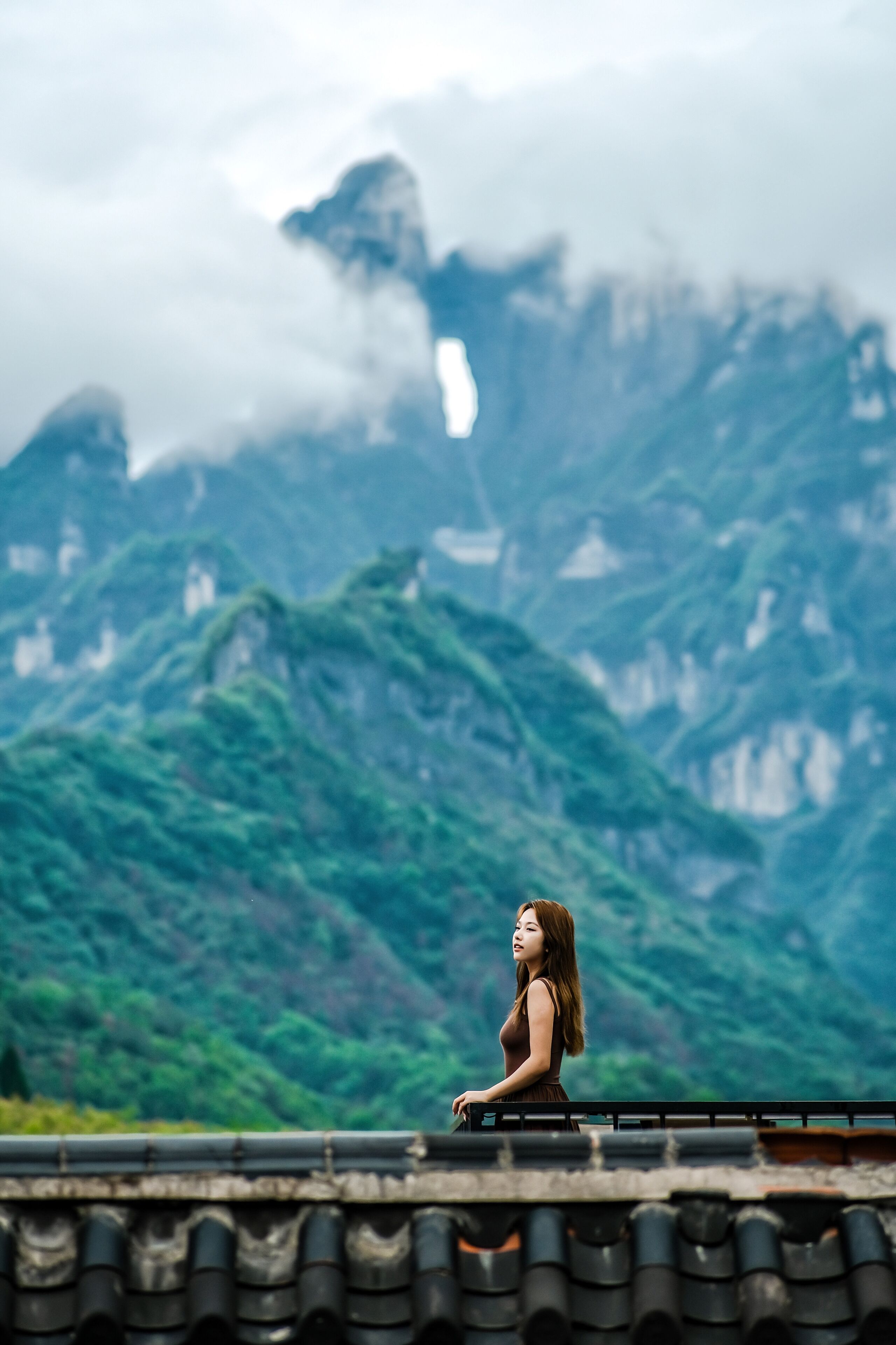 A person sitting on a roof overlooking a mountainous landscape.