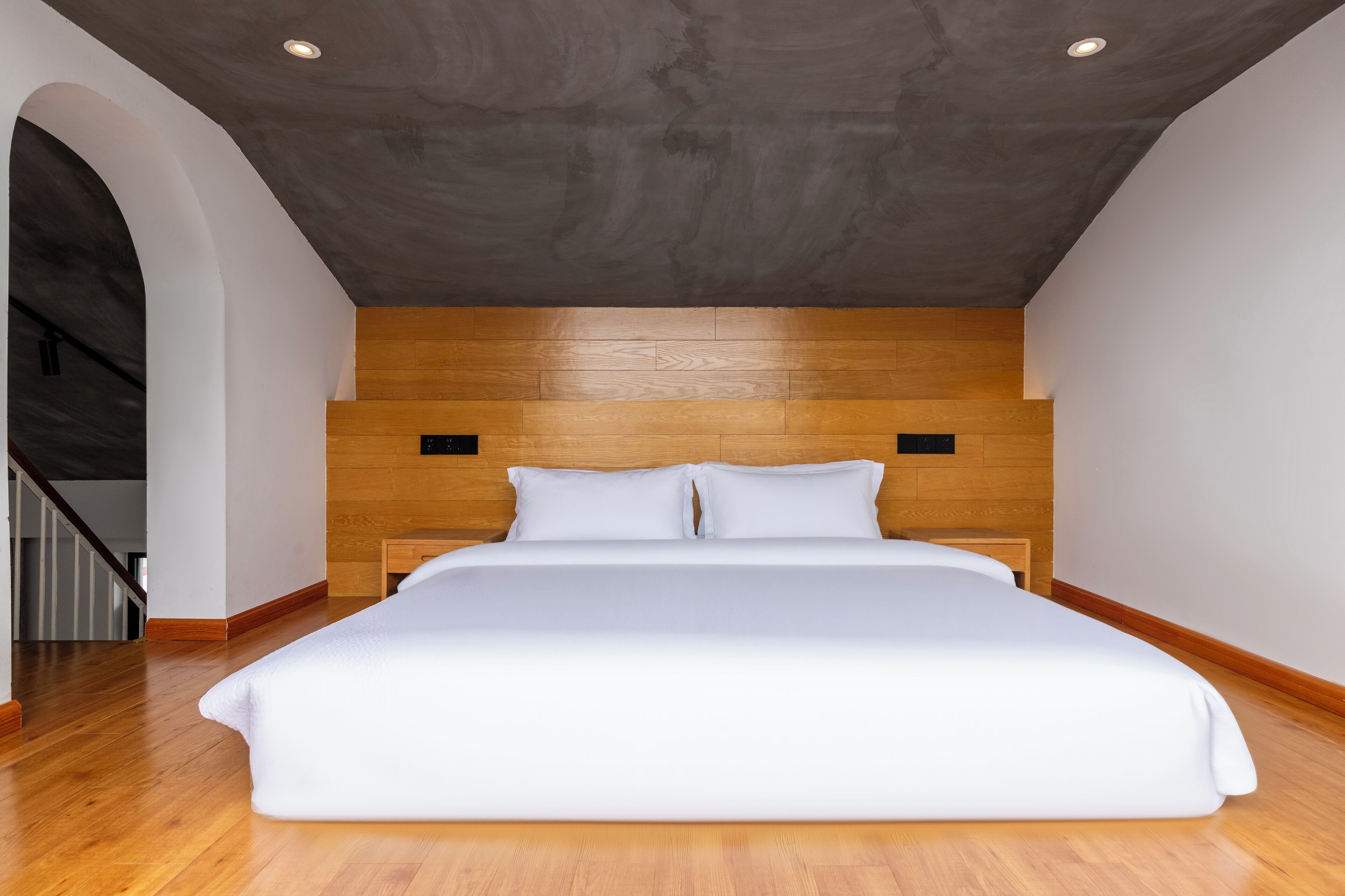 A modern bedroom with a large bed, wooden headboard, and a concrete ceiling.