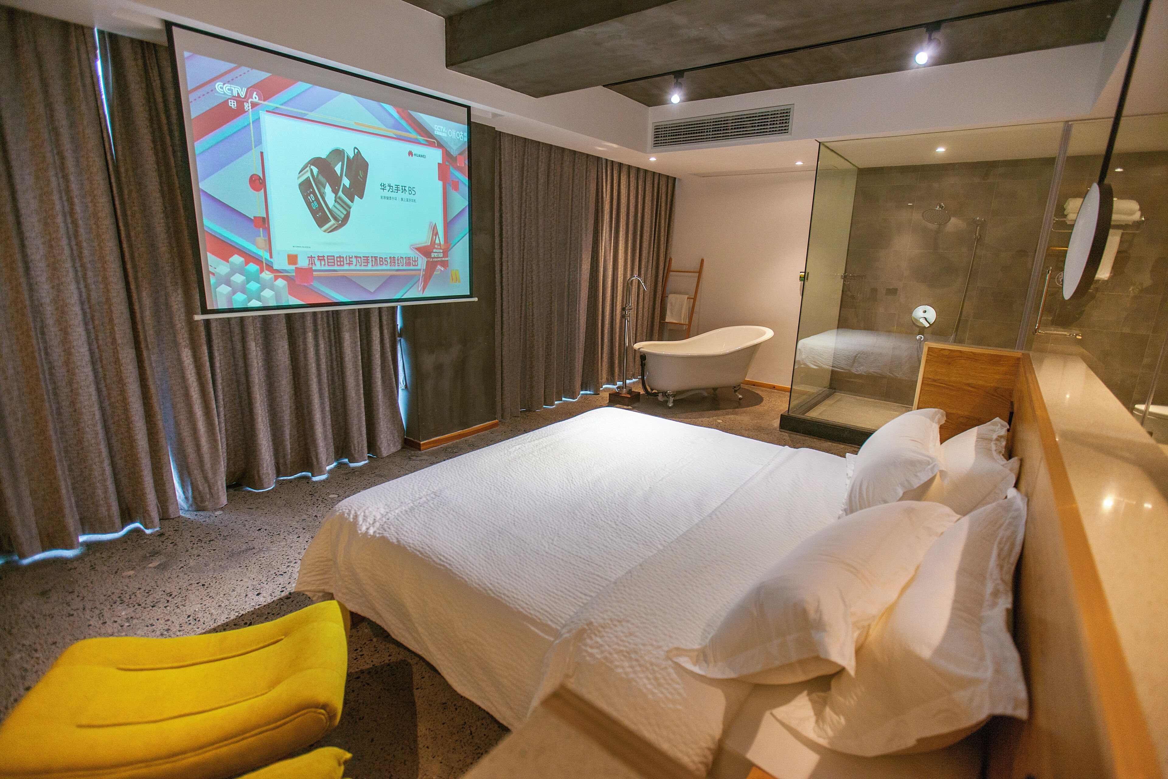 Une chambre d’hôtel avec un grand lit, une baignoire, une douche et une chaise jaune.