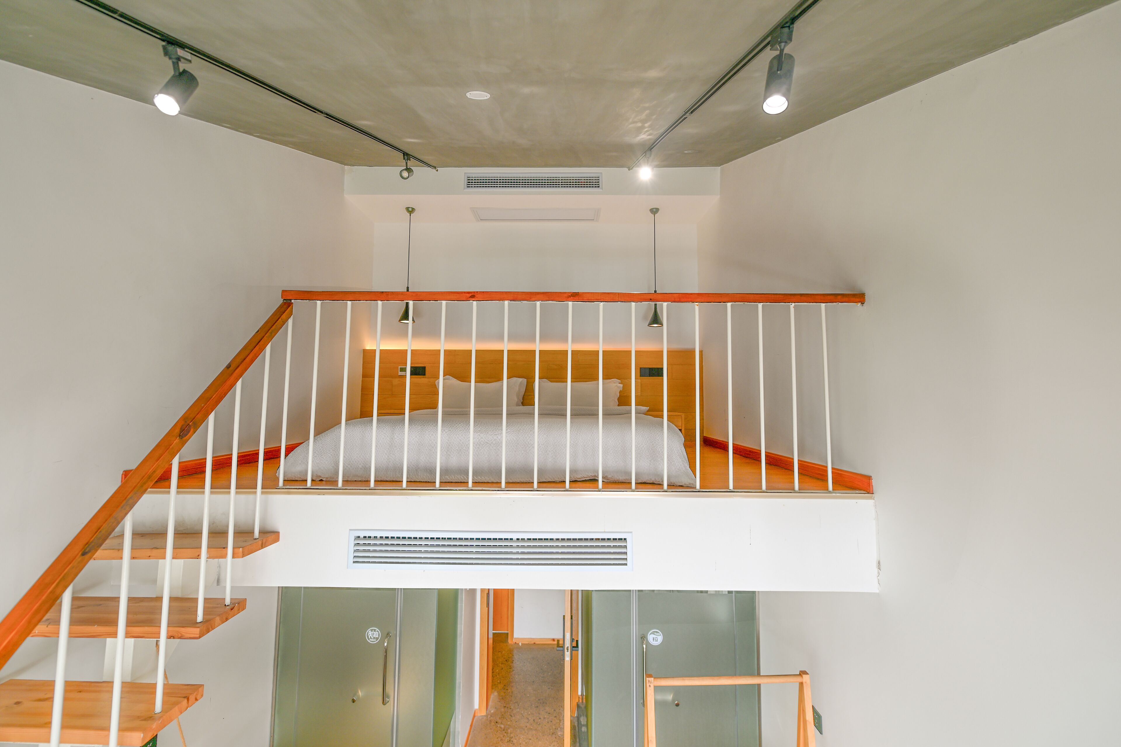 A loft bedroom with a wooden staircase, a bunk bed, and a small desk area.