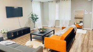 En moderne stue med et fladskærms-tv, en sofa, et sofabord og en potteplante.