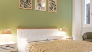 Een slaapkamer met een bed, twee nachtkastjes, een stoel en een kunstwerk aan de muur.