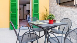 Een buitenterras met een tafel, stoelen, een potplant en een groene deur.