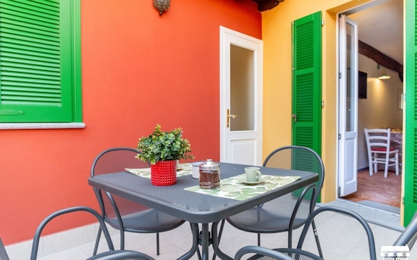 An outdoor patio with a table and chairs, a potted plant, and a door leading to an interior space. - Discover the unparalleled comfort of this charming apartment located in the beating heart of Bellano. Just steps from the lake and with the train station a short walk away, your home will be an oasis of tranquility and accessibility. With the ferry stop  (Bellano)