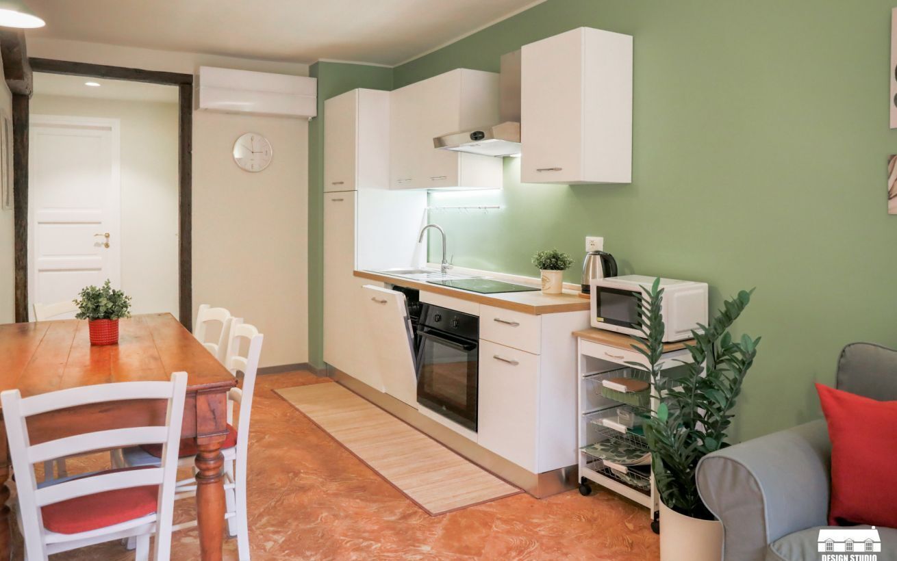A compact kitchen with white cabinets, a microwave, a sink, and a stove. There is a dining table with chairs and a small potted plant.