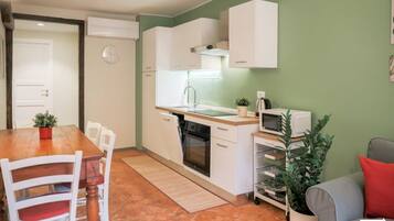 A compact kitchen with white cabinets, a microwave, a sink, and a stove. There is a dining table with chairs and a small potted plant.