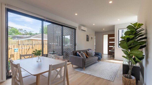 A modern living room with a dining area, large sliding glass doors to a backyard, and a potted plant.