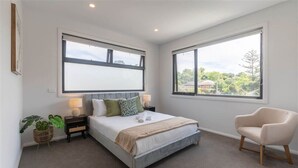 A bedroom with a bed, two bedside tables, a chair, and large windows.
