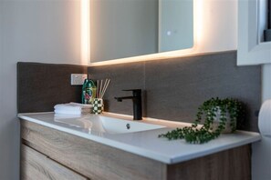 Une salle de bain moderne avec un lavabo blanc, un lambris mural foncé, un robinet noir et une petite plante verte posée sur le comptoir.