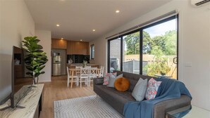 A modern kitchen with a dining area, a sofa with cushions, and a large window.
