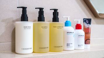 Uma prateleira no banheiro com diversos produtos de higiene pessoal, incluindo cuidados para cabelo, shampoo e produtos para a pele.