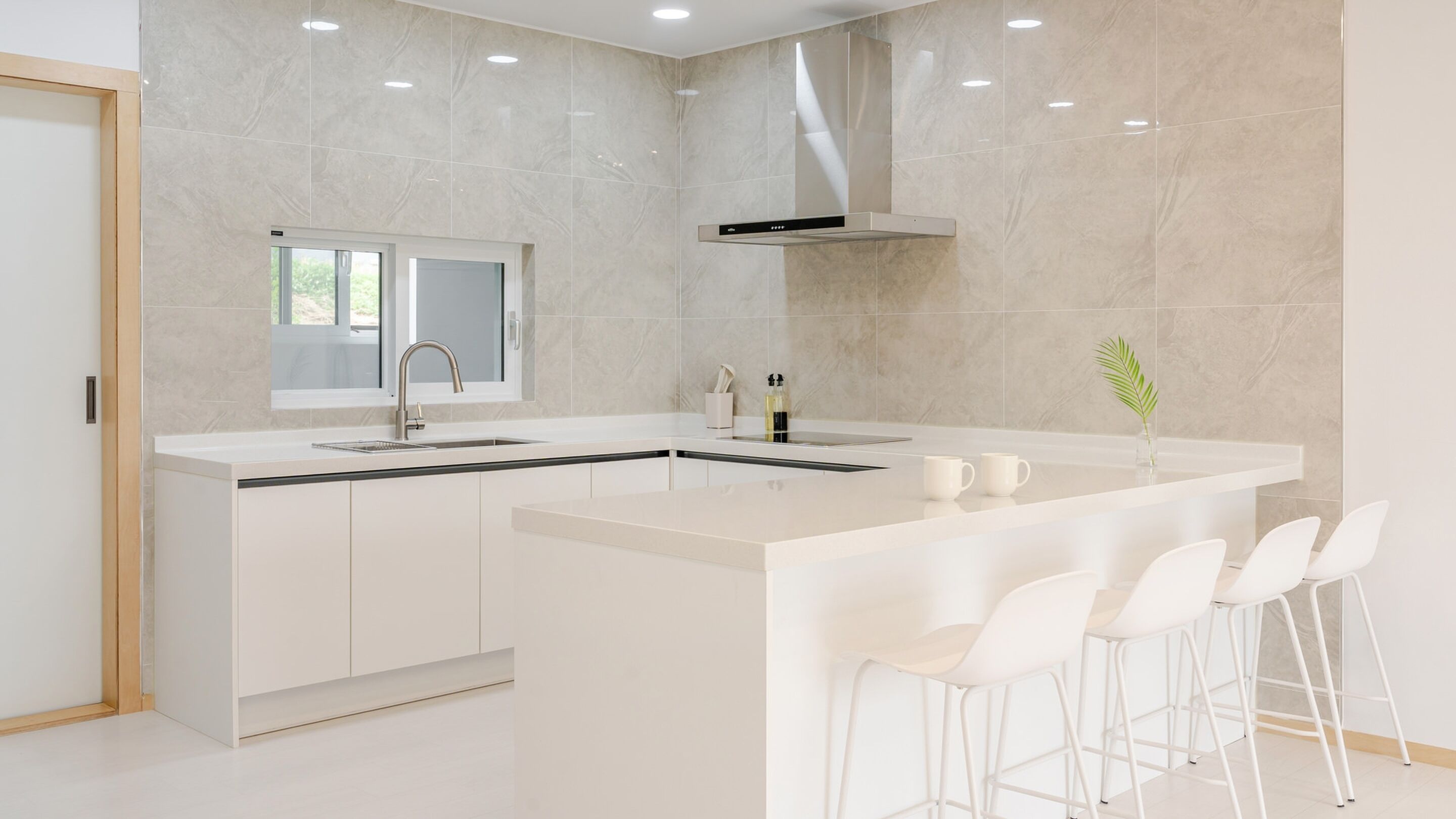 A modern kitchen with a large island, white bar stools, and a window above the sink.