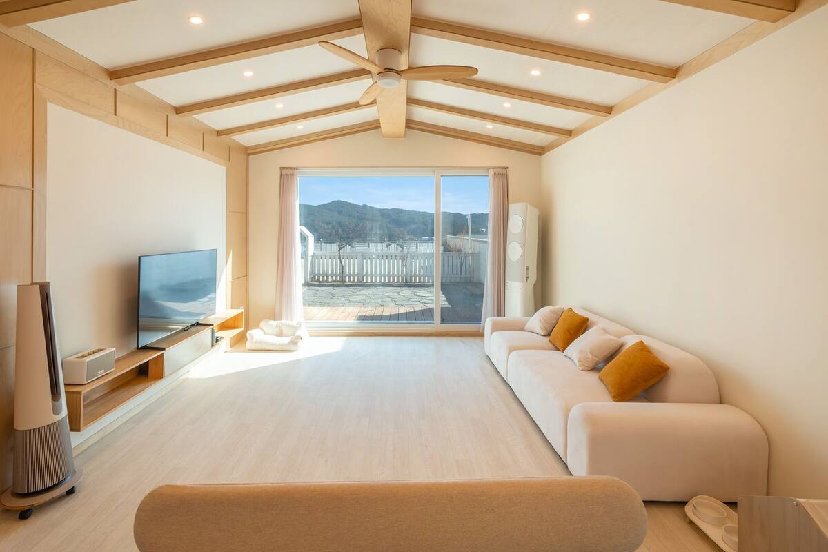 A modern living room with a flat-screen TV, a sofa, and a wooden ceiling.