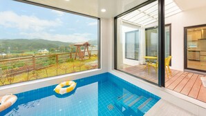 A modern indoor swimming pool with a clear view of a wooden deck and a small wooden structure.