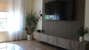 Een moderne woonkamer met een grote flatscreen televisie bevestigd aan een houten paneelwand, een potplant en een ronde glazen tafel.