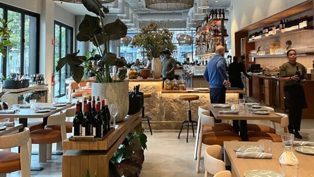 Een restaurant interieur met hoge plafonds, hangende rieten lampen en een bar.